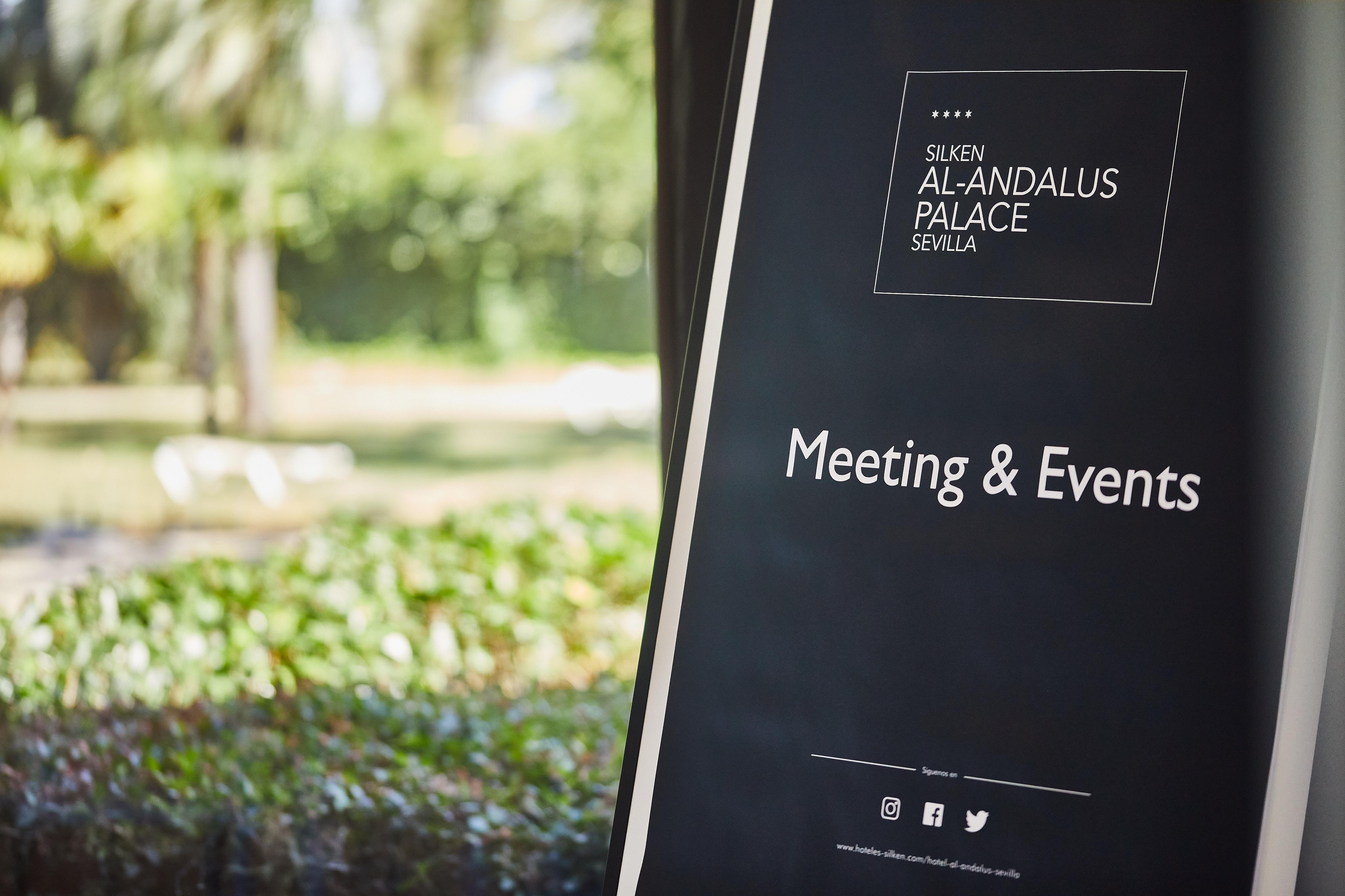 Silken Al-Andalus Palace Seville Exterior photo The photo displays a sign for "Silken Al-Andalus Palace" located in Seville. The sign is promoting "Meeting & Events" services. In the background, there are greenery and possibly some outdoor seating visible, suggesting a pleasant environment for eve