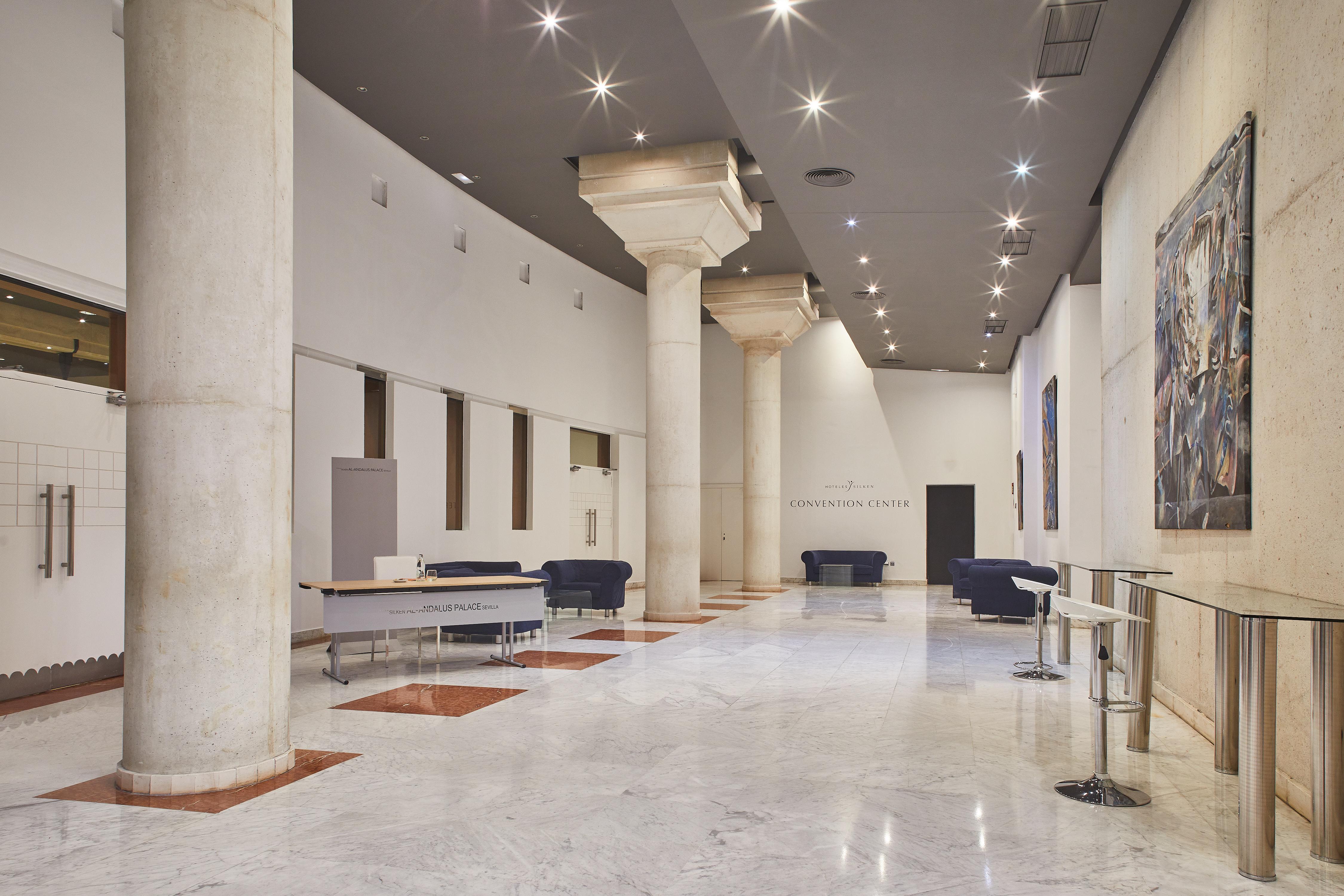 Silken Al-Andalus Palace Seville Exterior photo The photo shows a spacious interior, possibly a lobby or gallery, characterized by high ceilings and white walls. Large, cylindrical columns are present, supporting the structure. The floor appears to be made of polished marble, enhancing the sense o